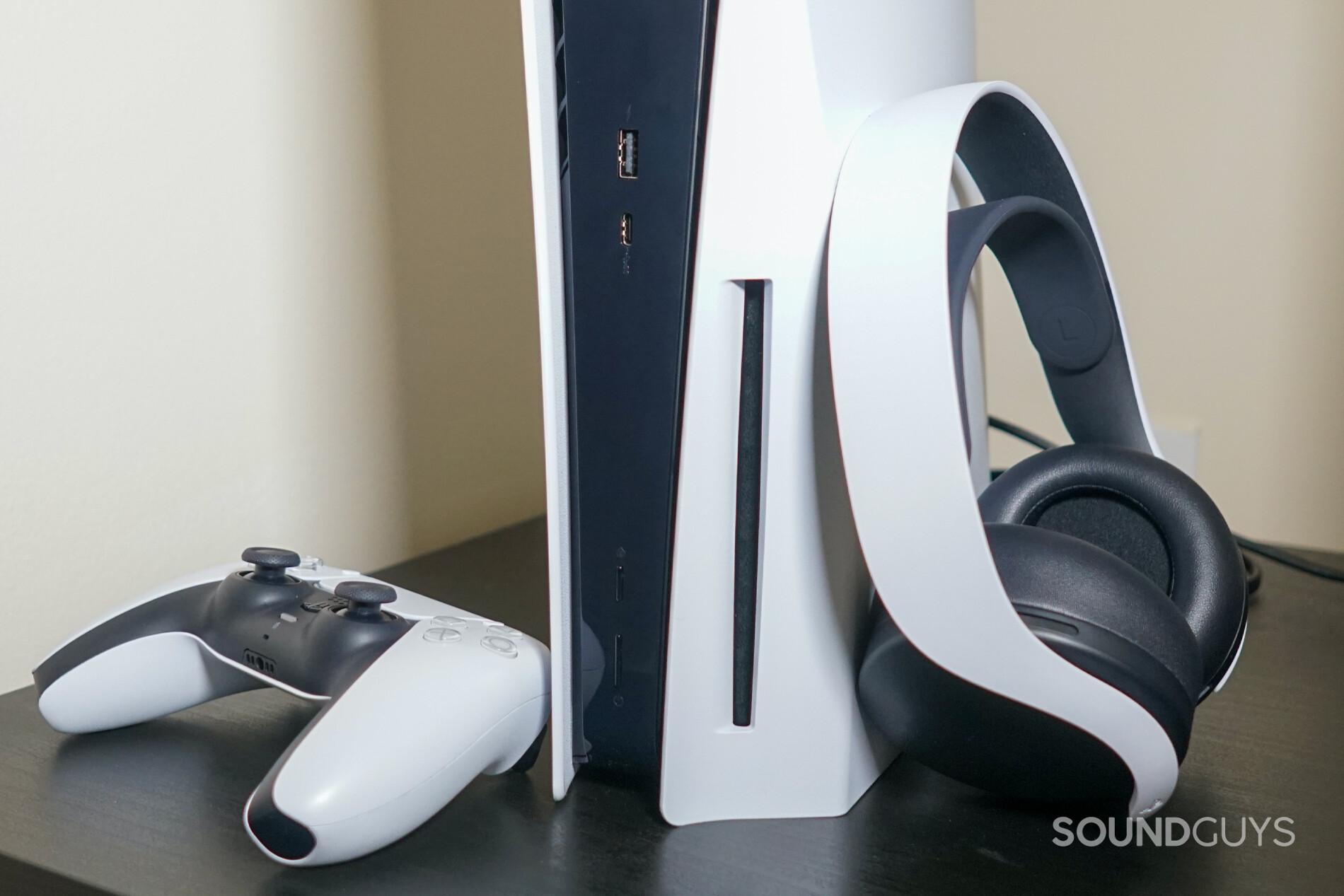 The Sony Pulse 3D Wireless Headset leans against a vertical Sony PlayStation 5 console, next to a PlayStation DualSense controller.