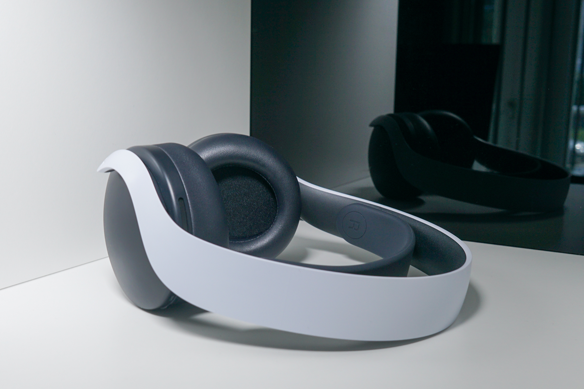 The Sony Pulse 3D Wireless Headset lays on a white shelf in front of a black reflective surface.