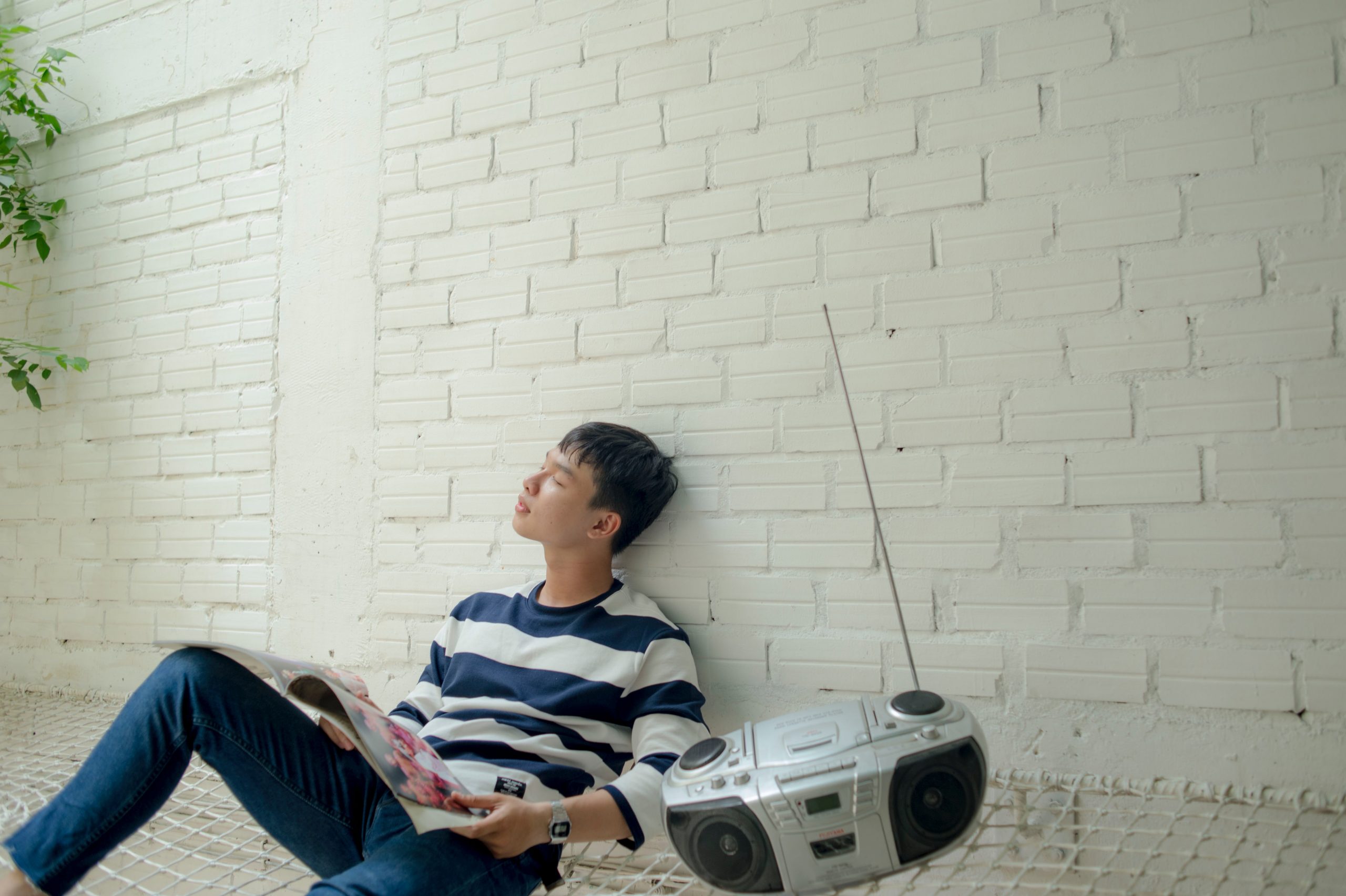 A man sitting against a brick wall holding a vinyl record. A radio and CD player rests next to him.