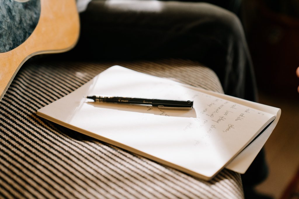 A notebook and pen on a bed. The side of a guitar is slightly visible.