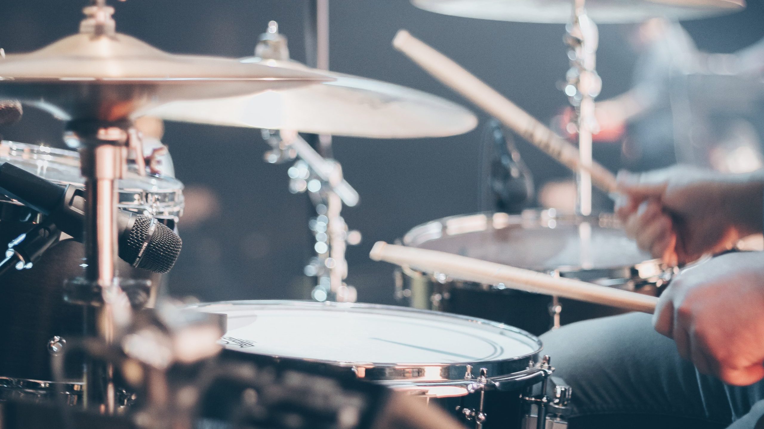 Hands holding drum sticks playing a drum kit.