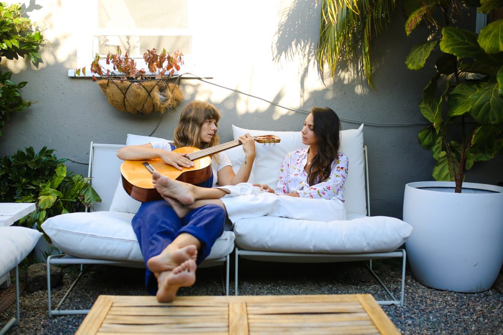 Two women sitting on an outdoor couch. One woman is playing guitar.