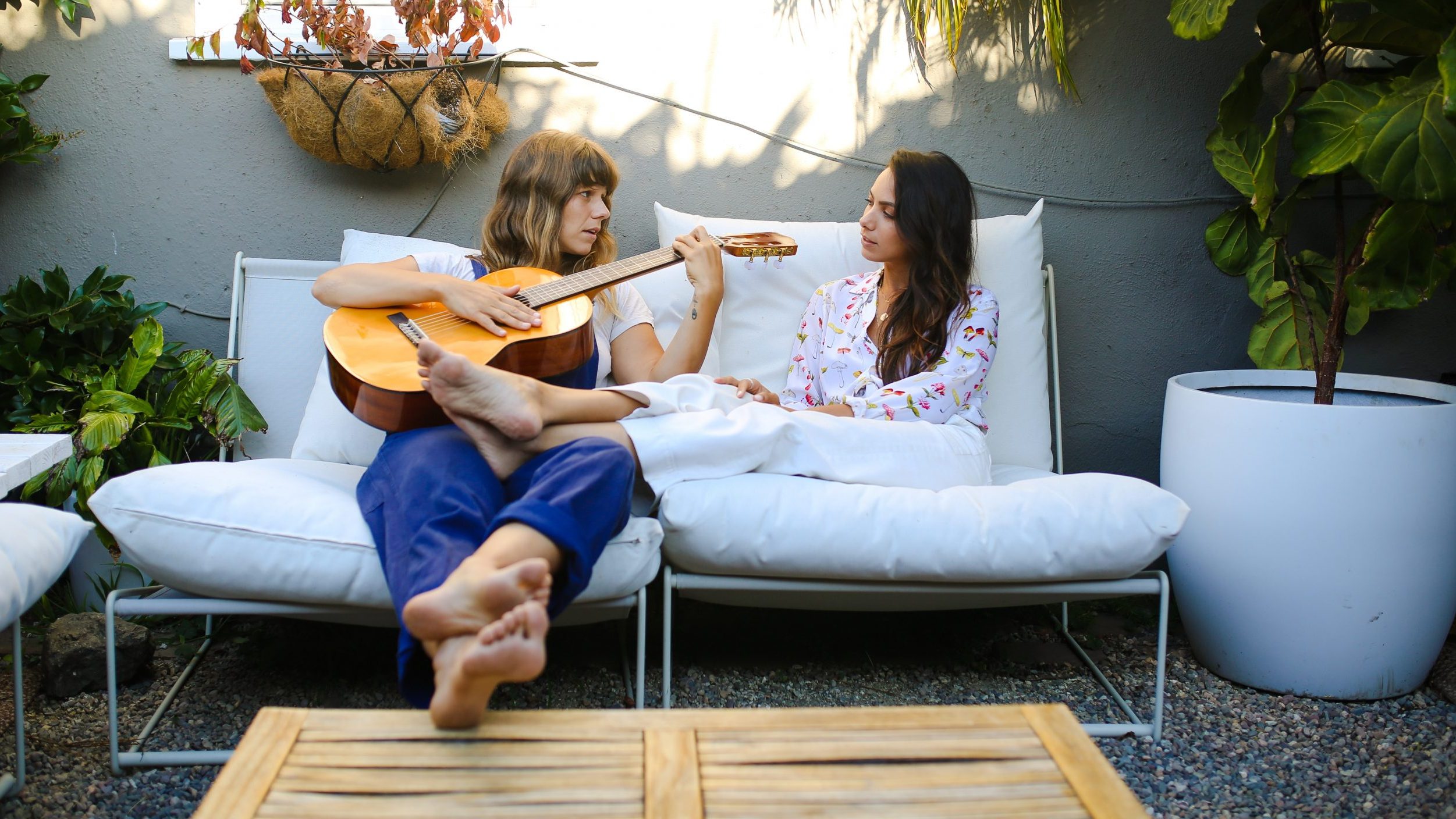 Two women sitting on an outdoor couch. One woman is playing guitar.