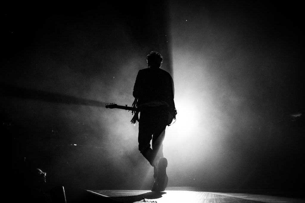 The silhouette of a man on stage as a light brightly backlights him.
