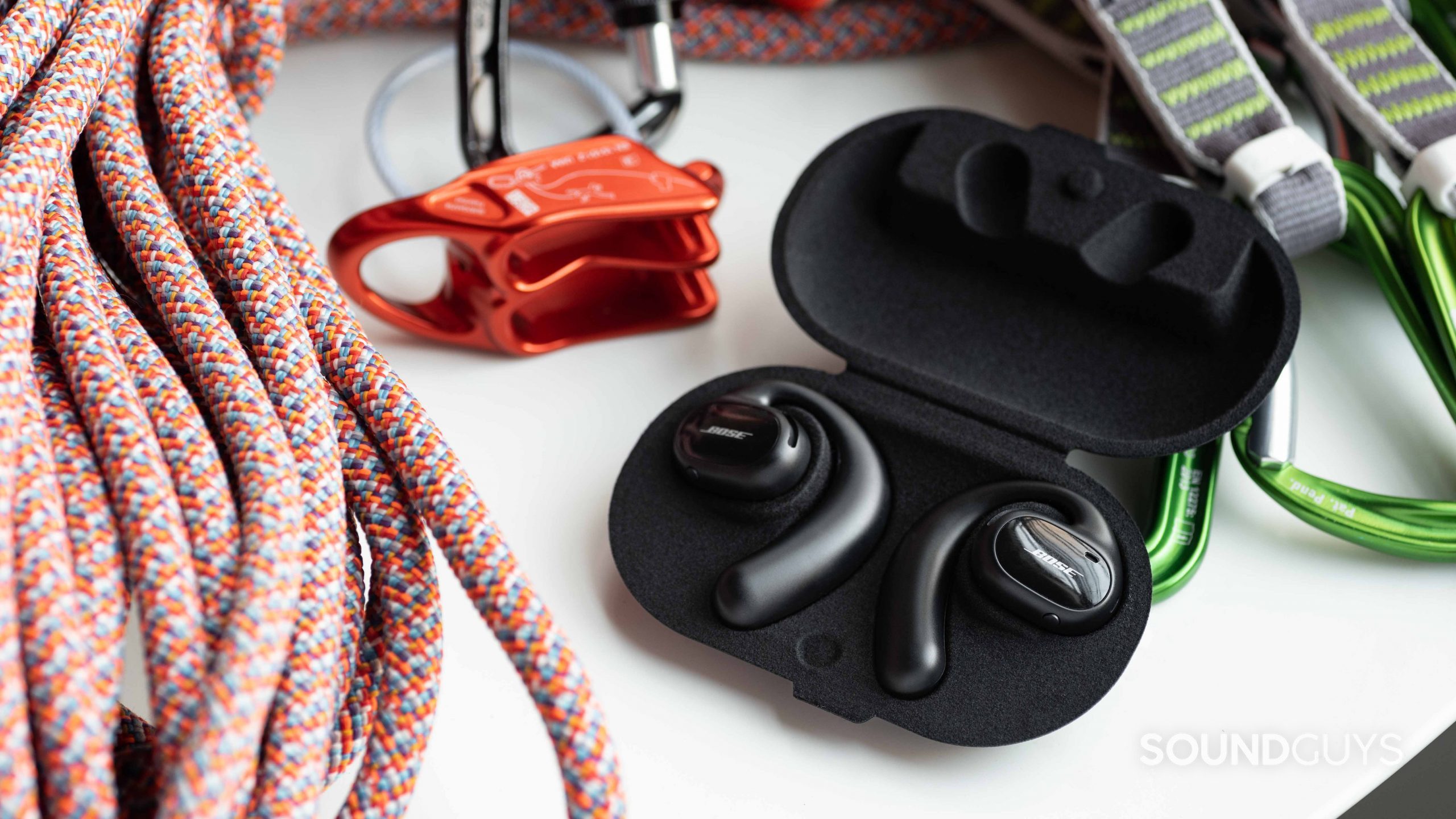 The Bose Sport Open Earbuds in the open carrying case next to a climbing rope and belay device.