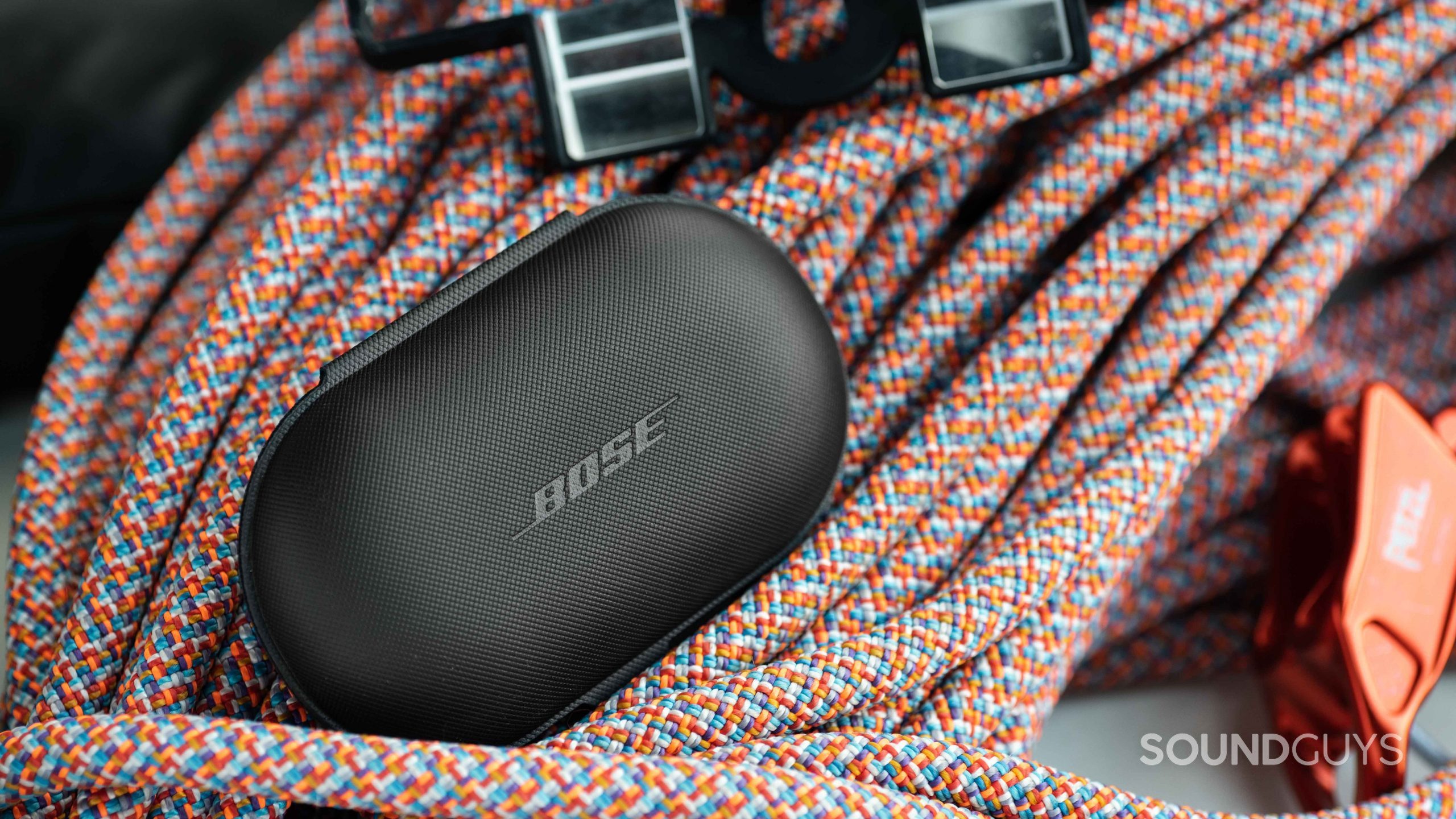 The Bose Sport Open Earbuds textured carrying case sits on top of a rock climbing rope.
