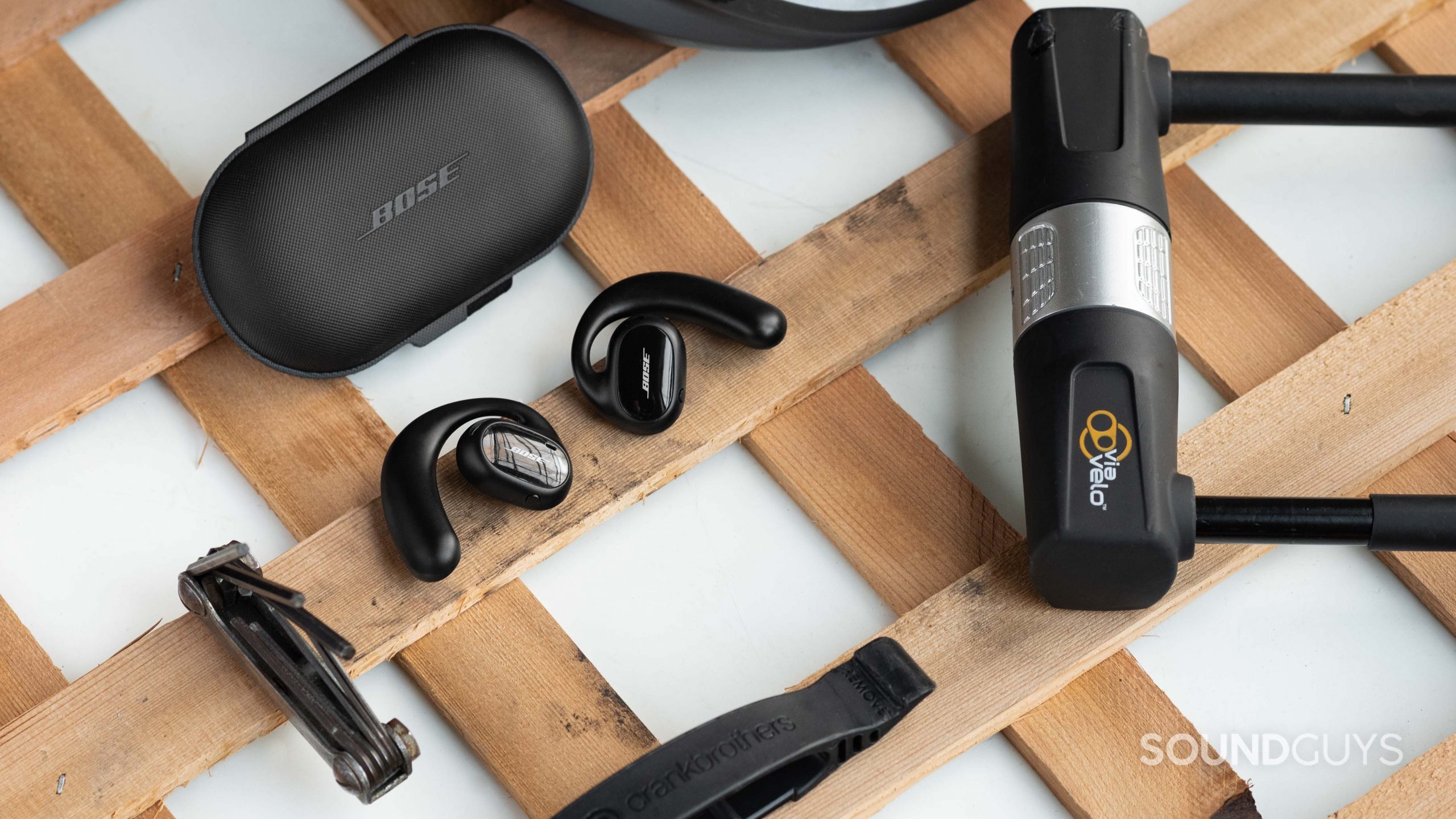 The Bose Sport Open Earbuds outside of the closed carrying case and surrounded by bike tools.