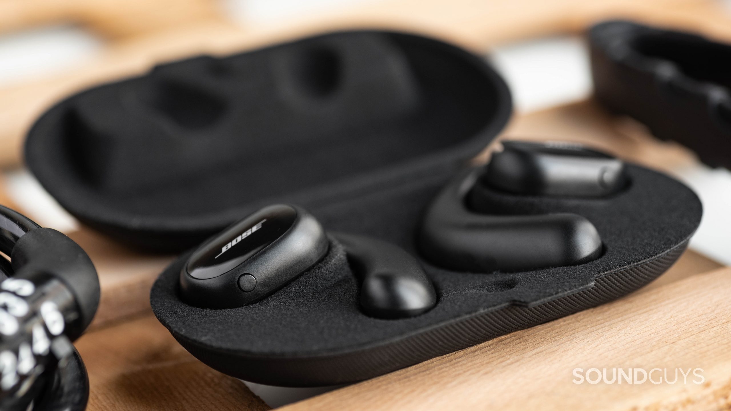 The Bose Sport Open Earbuds in the open case with the left earbud button in clear view.