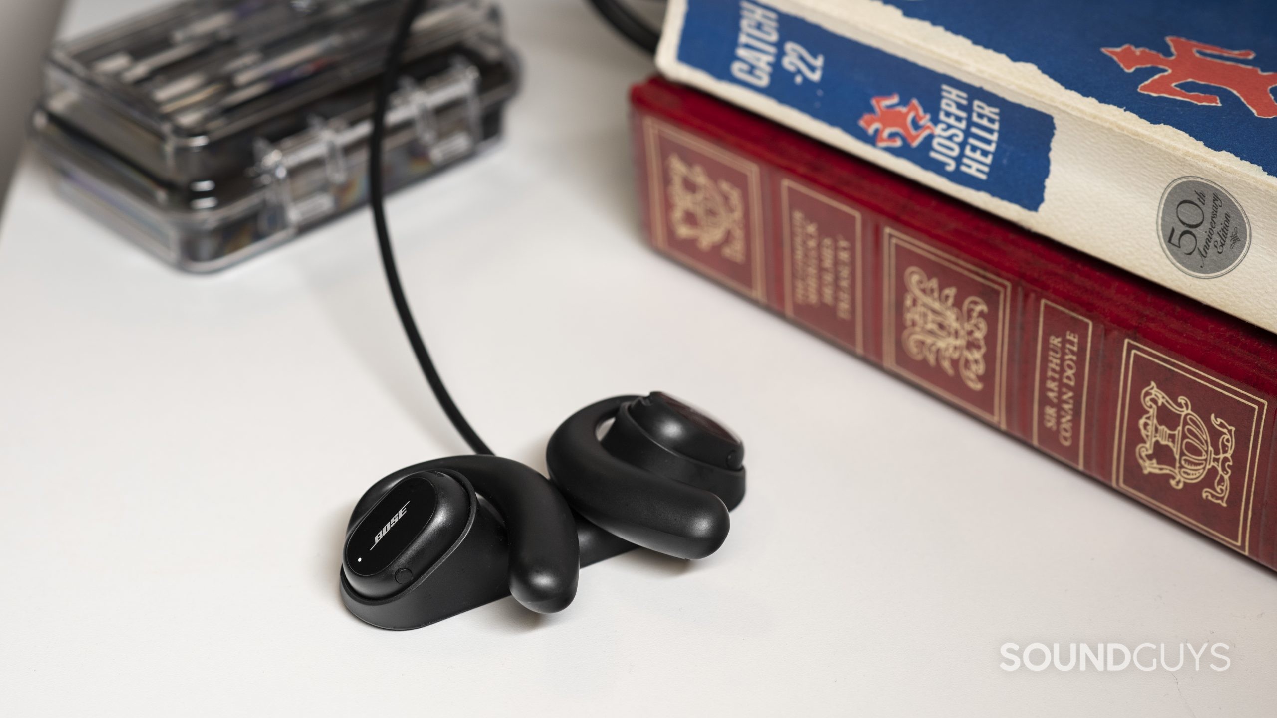 The Bose Sport Open Earbuds secured in the proprietary charging dock next to a stack of books.