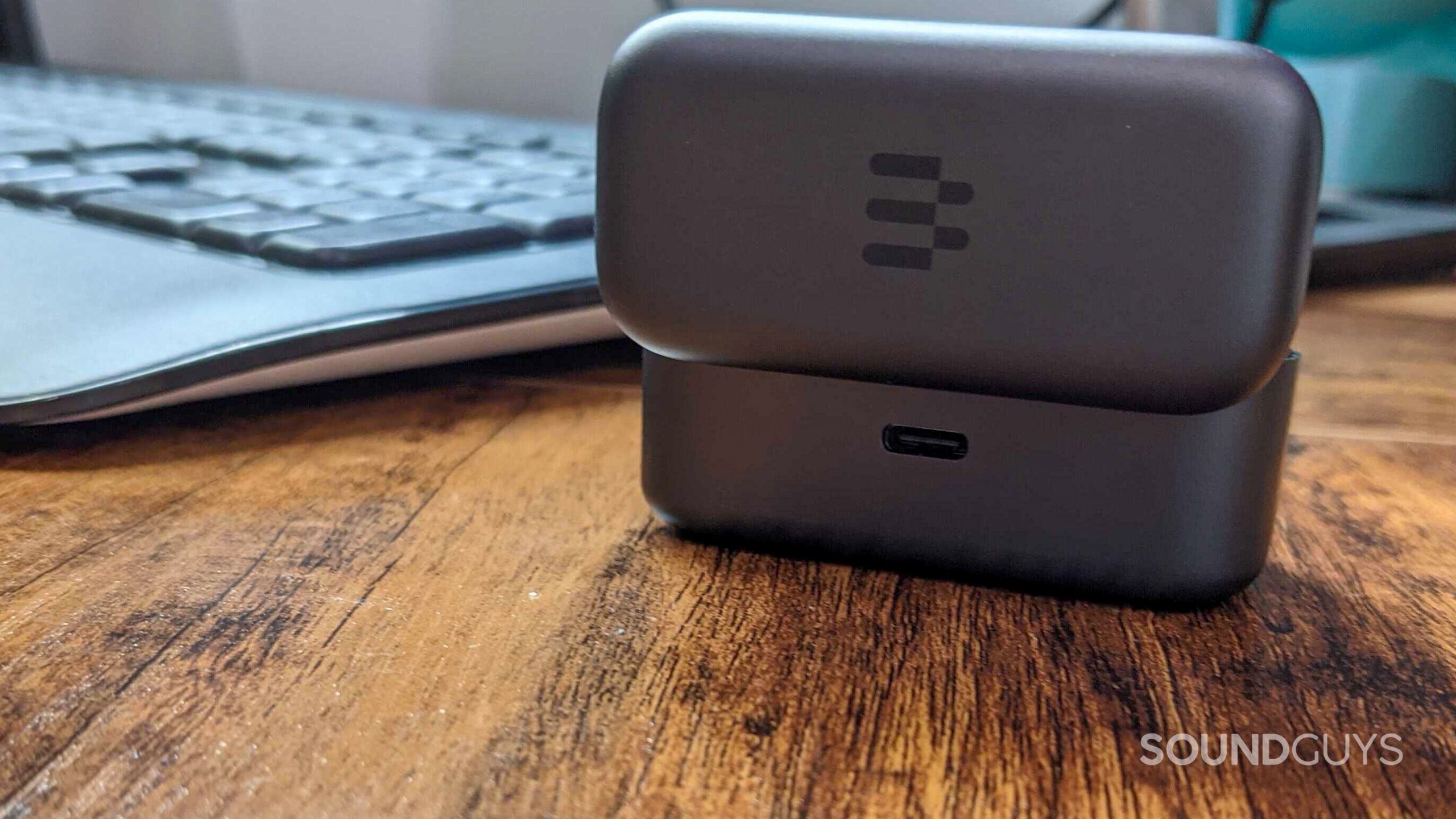 The EPOS GTW 270 Hybrid charging case sits on a wooden desk with its lid open, turned around to show its USB-C charging port.
