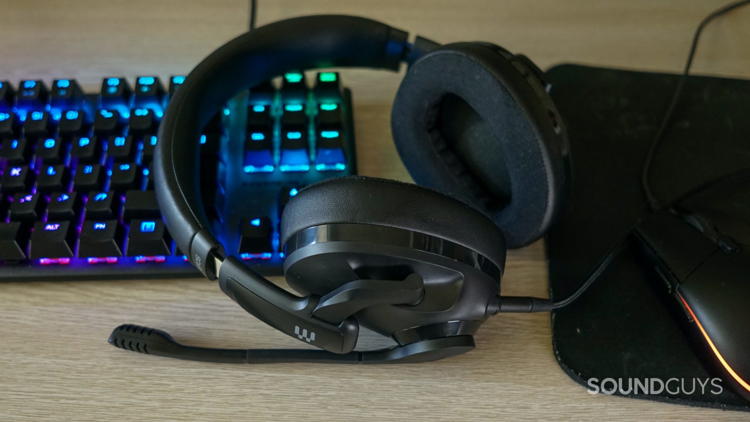 The EPOS H3 gaming headset lays on a desk next to a HyperX Alloy Origins mechanical gaming keyboard and Logitech Hero gaming mouse.