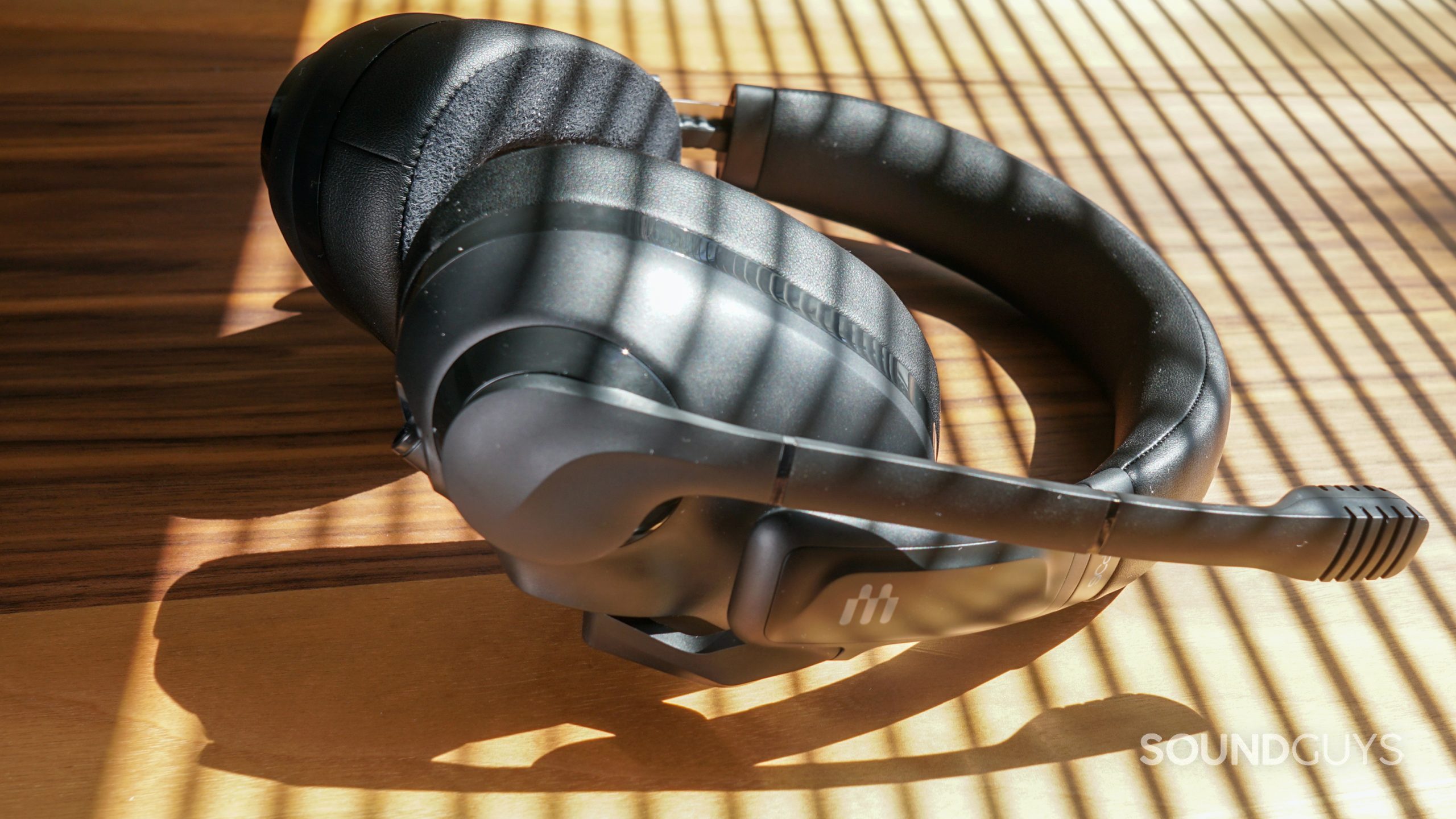 The EPOS H3 gaming headset lays on a wooden table with sunlight streaming in through drawn blinds