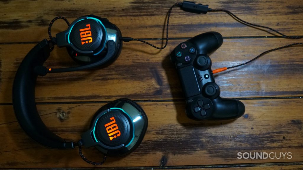 THe JBL Quantum lays on a wooden table plugged into the headphone jack of a PlayStation DualShock 4 controller.