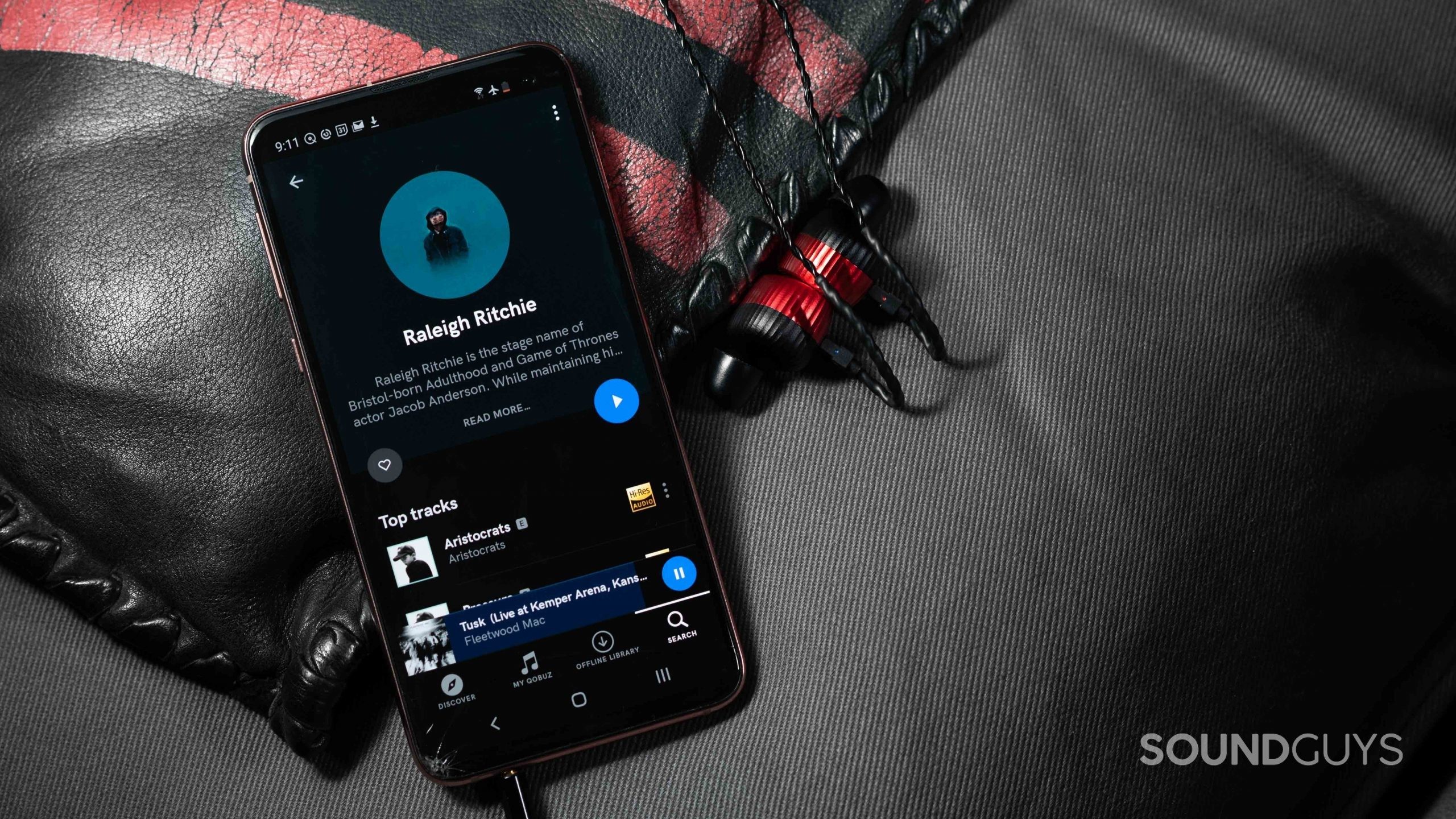 The Qobuz music streaming service app's Artist page open on a Samsung Galaxy S10e smartphone with red Noble Kaiser 10 IEMs next to the phone.