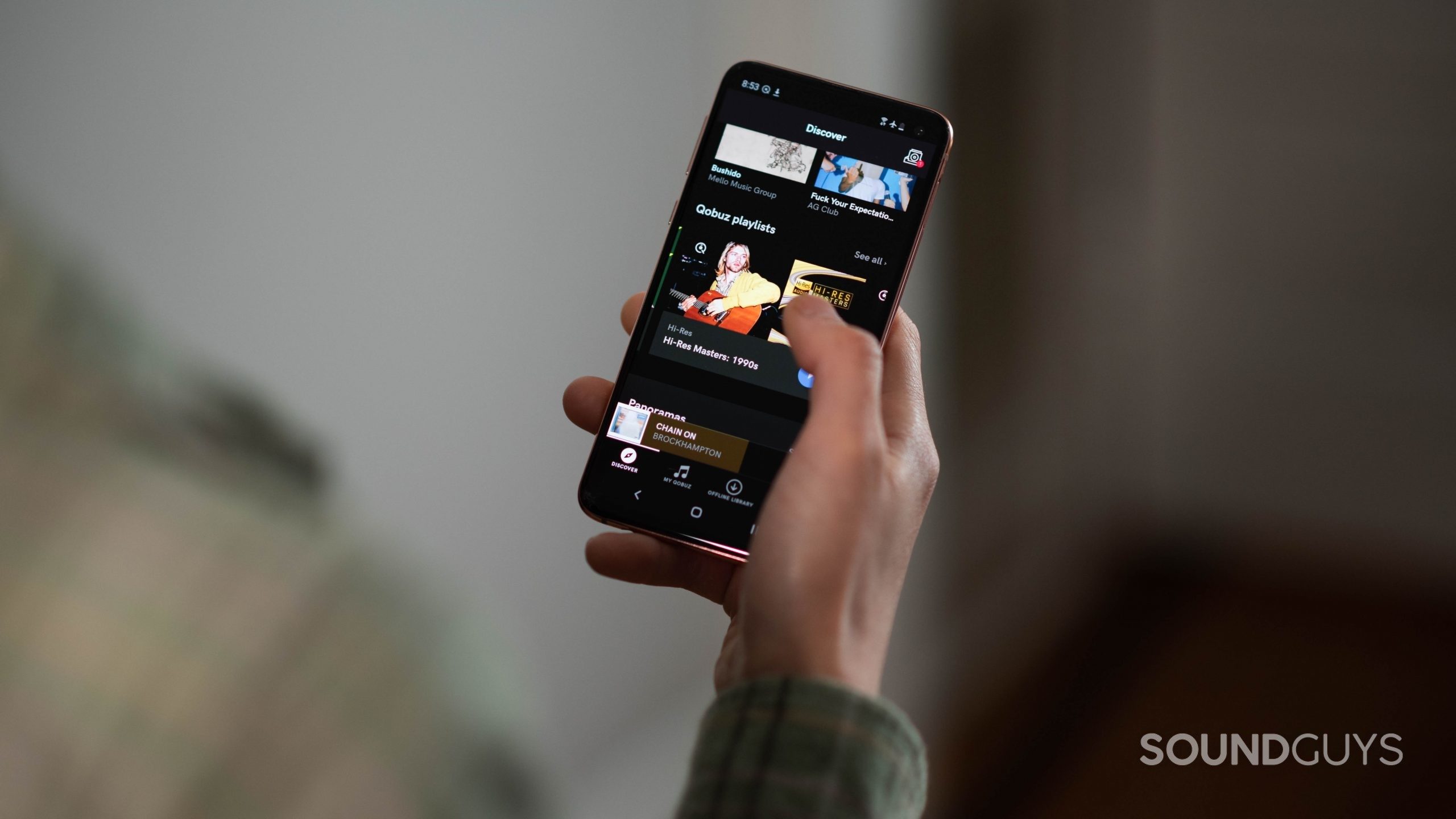 A woman holds a Samsung Galaxy S10e with the Qobuz Discovery page on display.