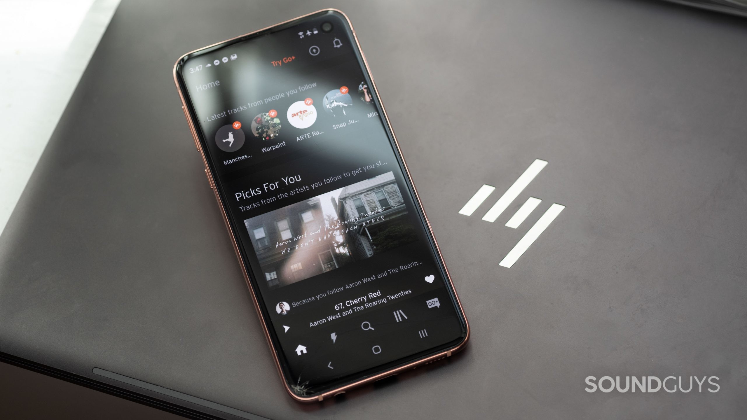 The SoundCloud mobile app open on an Android smartphone as it rests on top of an HP laptop.