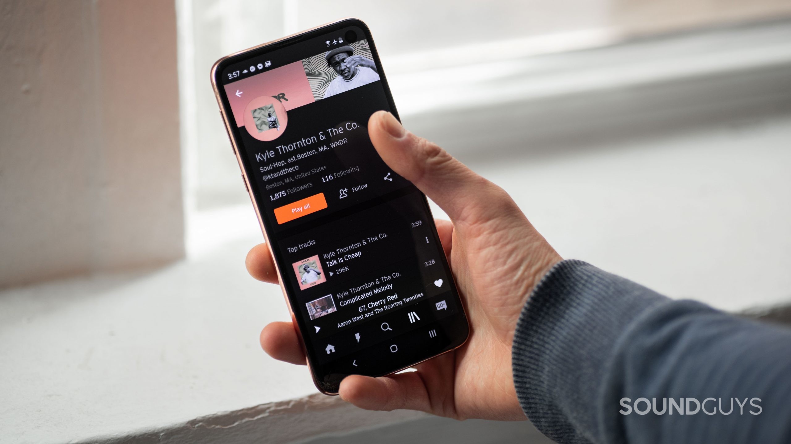 A hand holds a smartphone with the Spotify app open to a specific artist page.