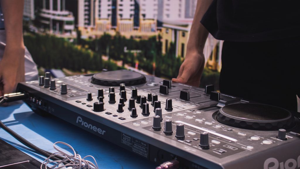 A person in a black T-shirt stands in front of a Pioneer DJ mixer.