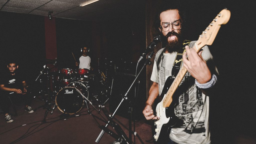 A three-person rock band rehearses in a studio.