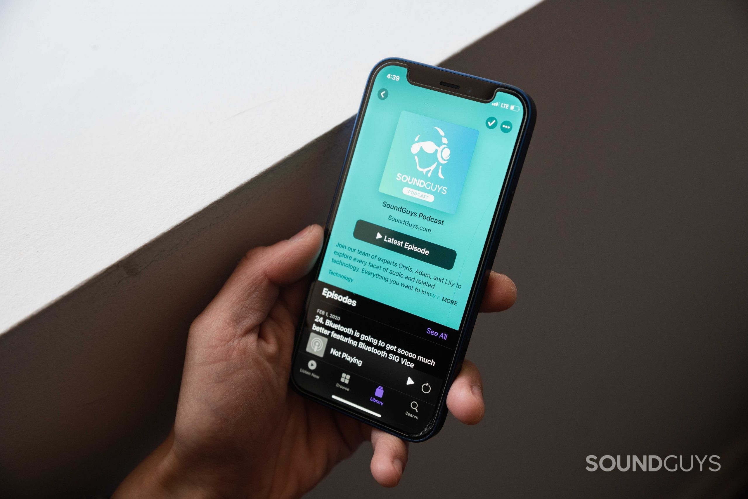 A hand holds an iPhone 12 Mini with the Apple Podcasts app open to the SoundGuys Podcast page.