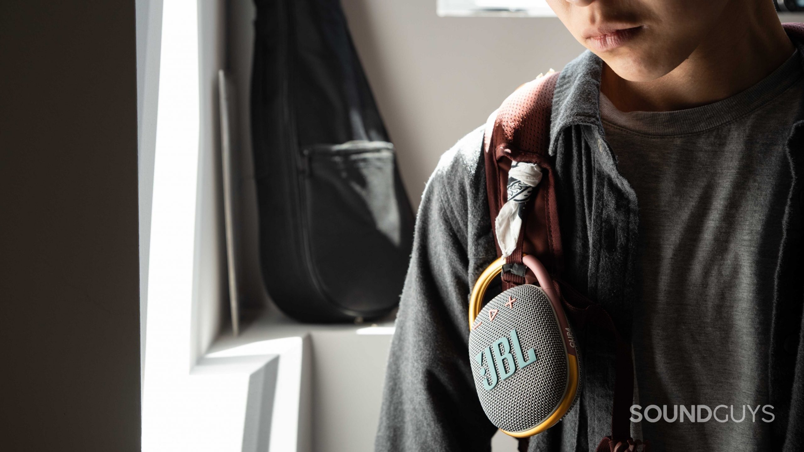 A woman wears the JBL Clip 4 speaker on her backpack strap.
