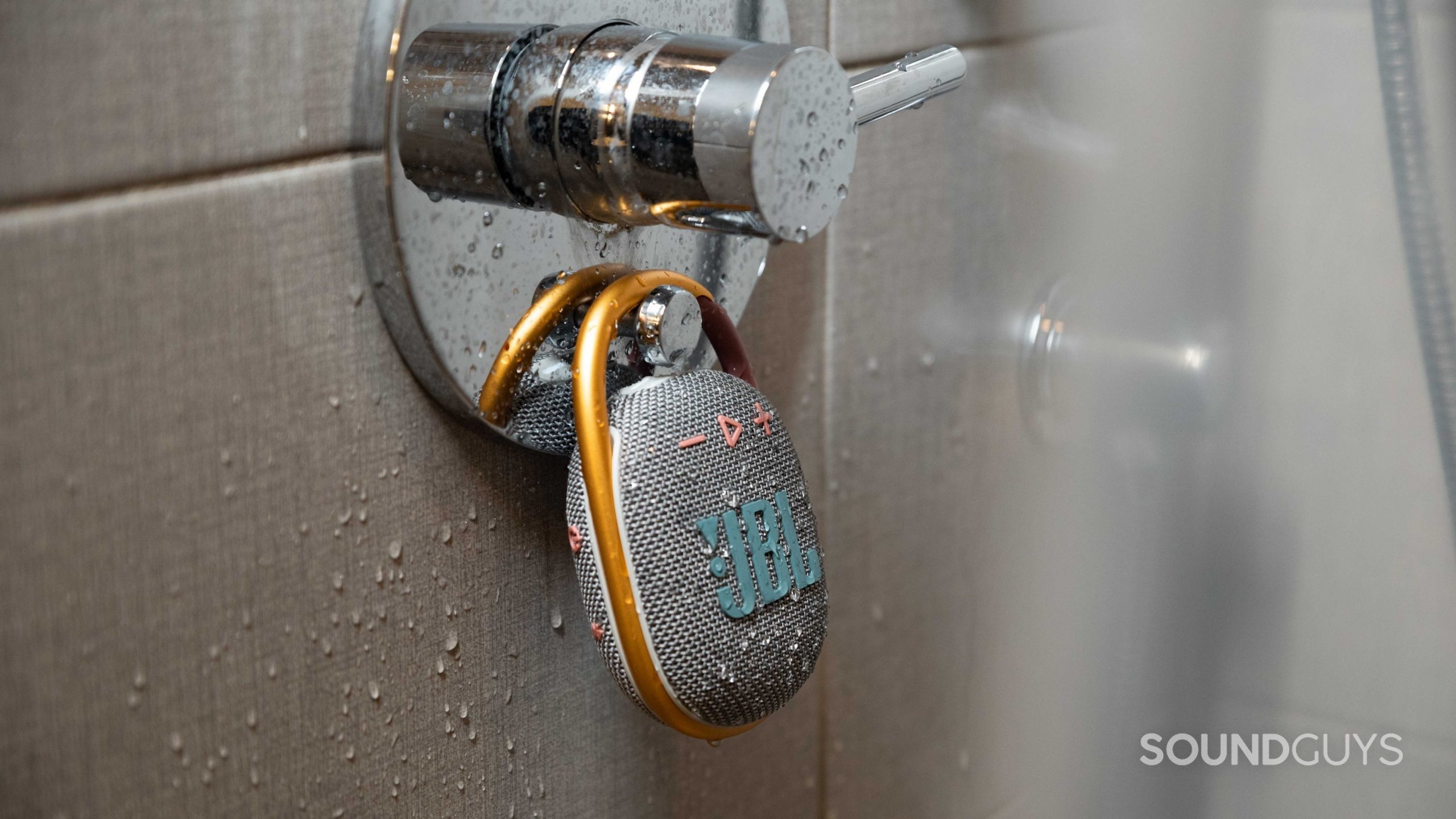 The JBL Clip 4 Bluetooth speaker hands from a shower as it's sprinkled by water.