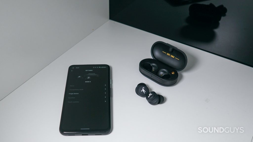 The Marshall Mode II true wireless earbuds sit outside their charging case next to a Google Pixel 4a runnin the Marshall Bluetooth app.