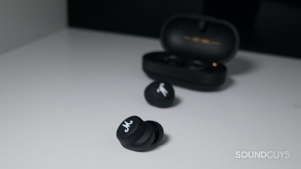 The Marshall Mode II true wireless earbuds sit in front of their charging case on a wide shelf in front of a reflective black surface