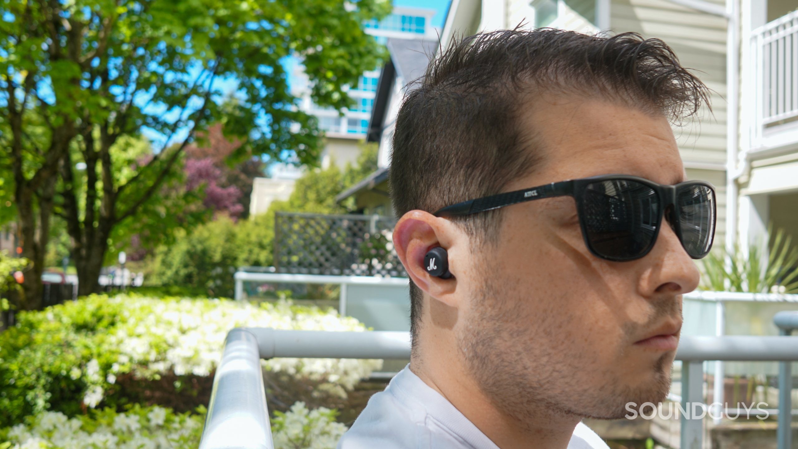 Marshall Mode II headshot A man sits outside wearing sunglasses and the Marshall Mode II true wireless earbuds.