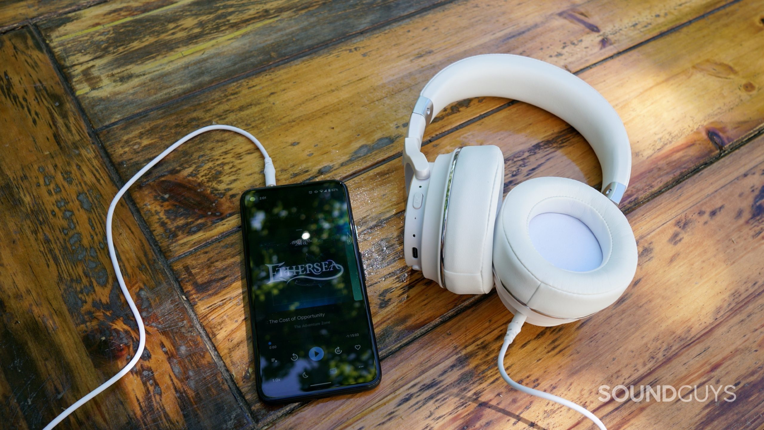 Raycon Everyday Headphones Pixel 4a 3.5mm The Raycon Everyday headphones lay on a wooden table connected over 3.5mm to a Google Pixel 4a playing The Adventure Zone
