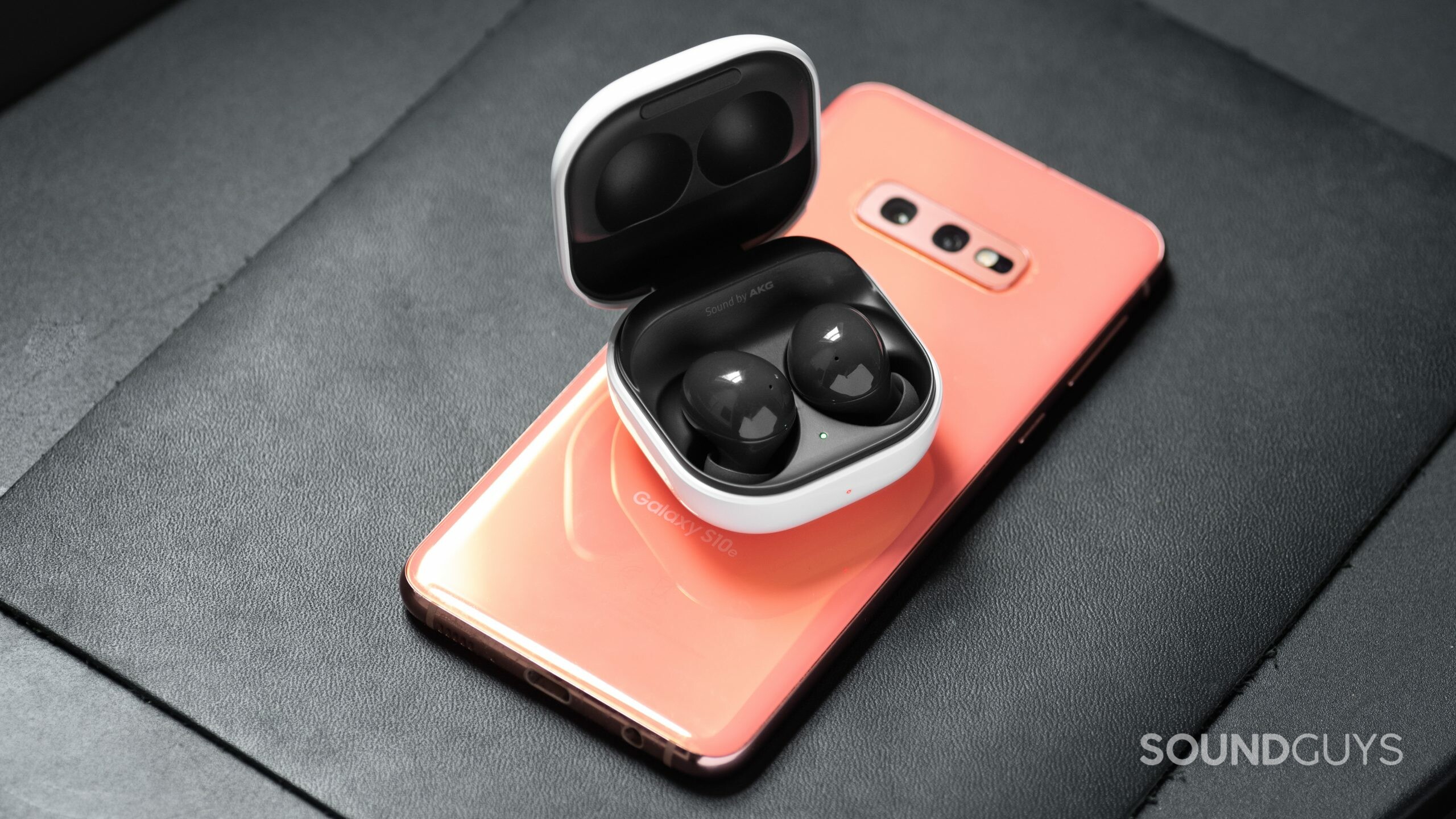 The Samsung Galaxy Buds 2 noise canceling true wireless earphones in the open charging case on top of a Samsung Galaxy S10e smartphone in pink.
