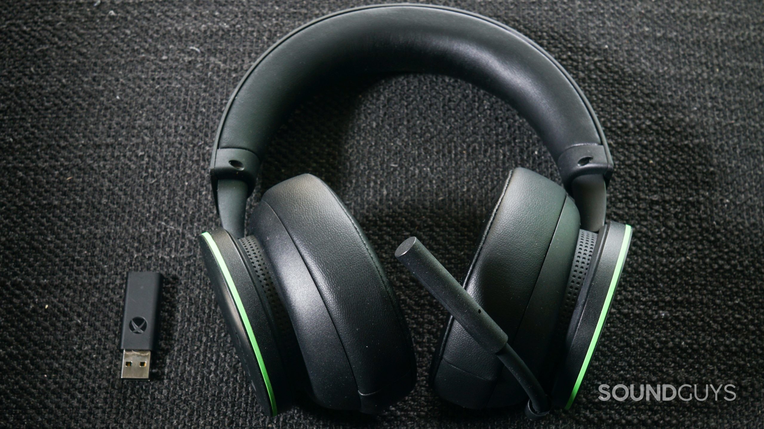 The Microsoft Xbox Wireless Headset lays on a fabric surface next to the Windows Xbox Wireless Adapter.