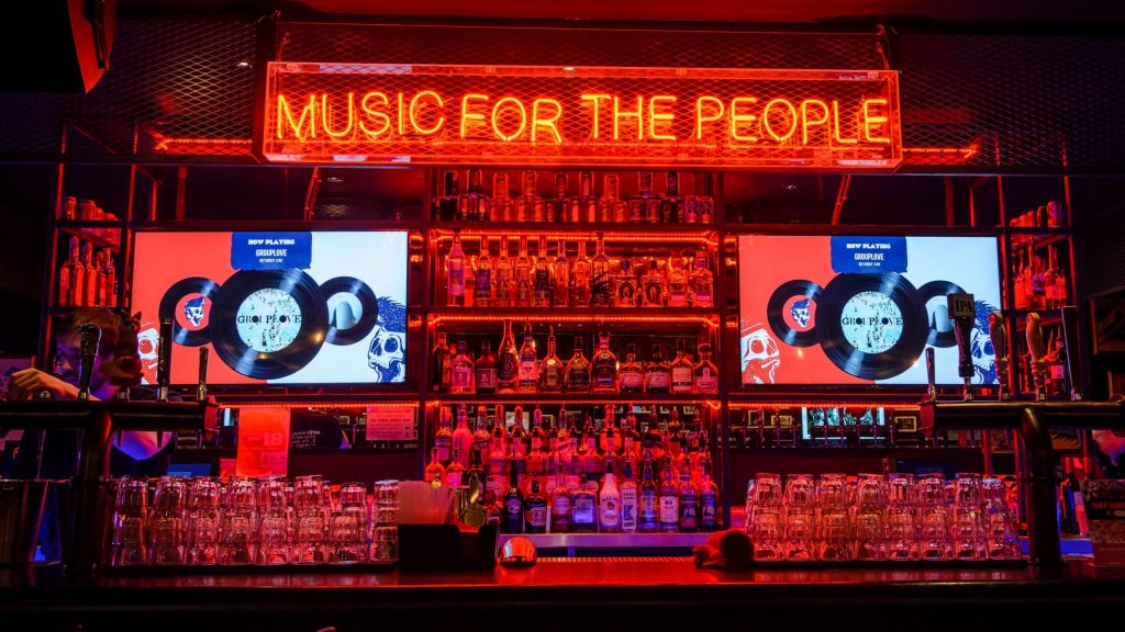 Neon sign on a wall that reads "music for the people", flanked by vinyl records