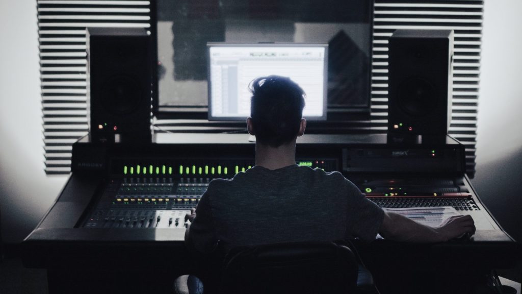 A man sits at a mixing console between a pair of speakers