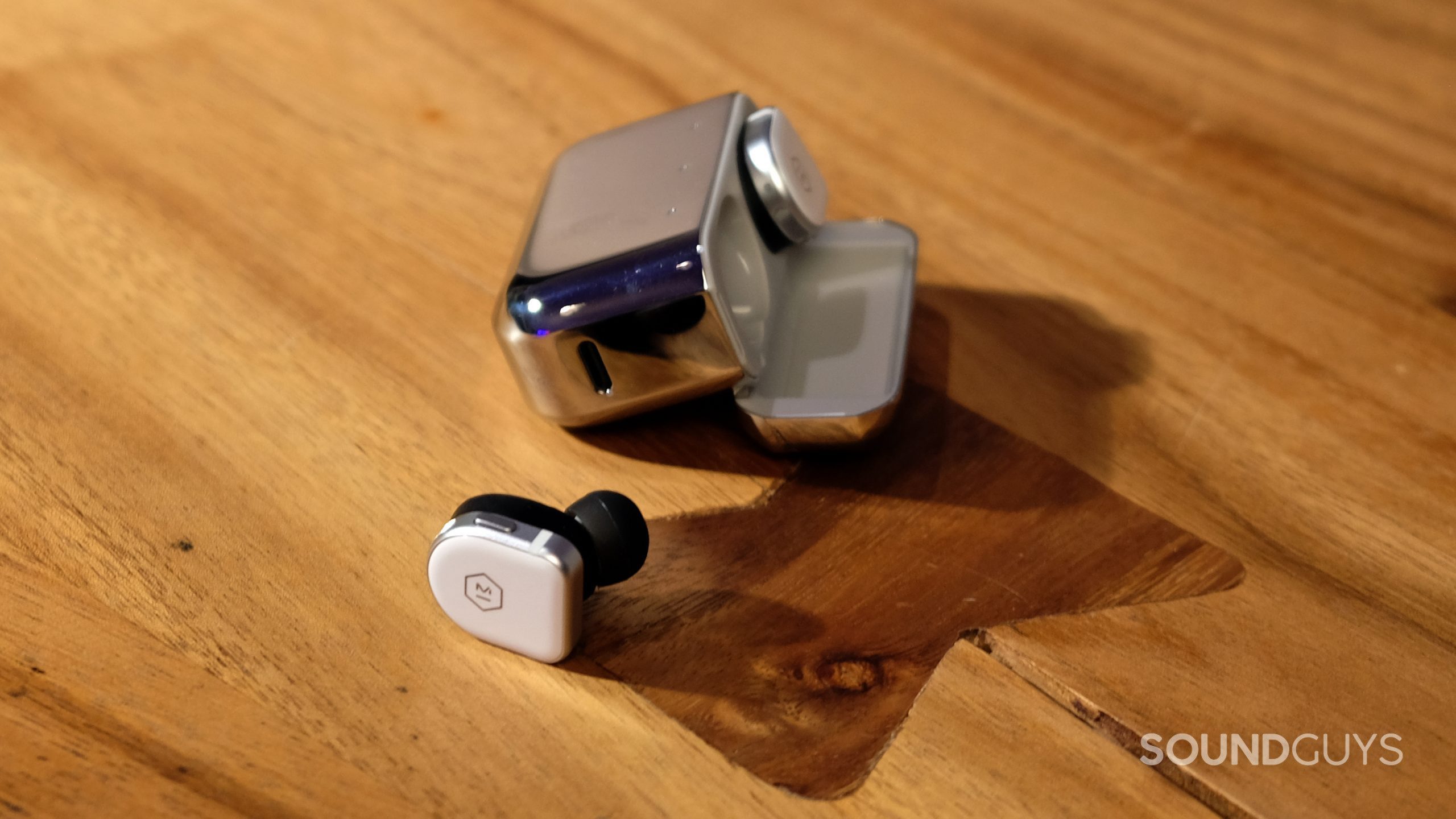 Sitting on a table there is a single master &amp; dynamic mw08 earbud, with the other in its case.