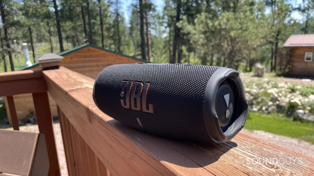 JBL Charge 5 resting on a balcony with a cabin and forest in the background.