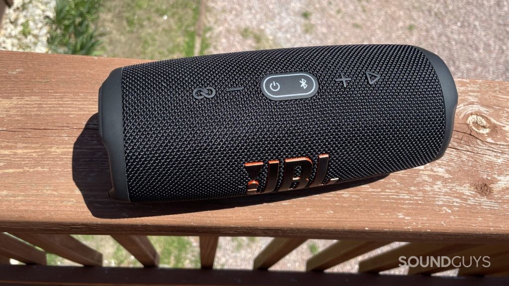 JBL Charge 5 resting on a balcony fence. The top buttons of the speaker are visible.