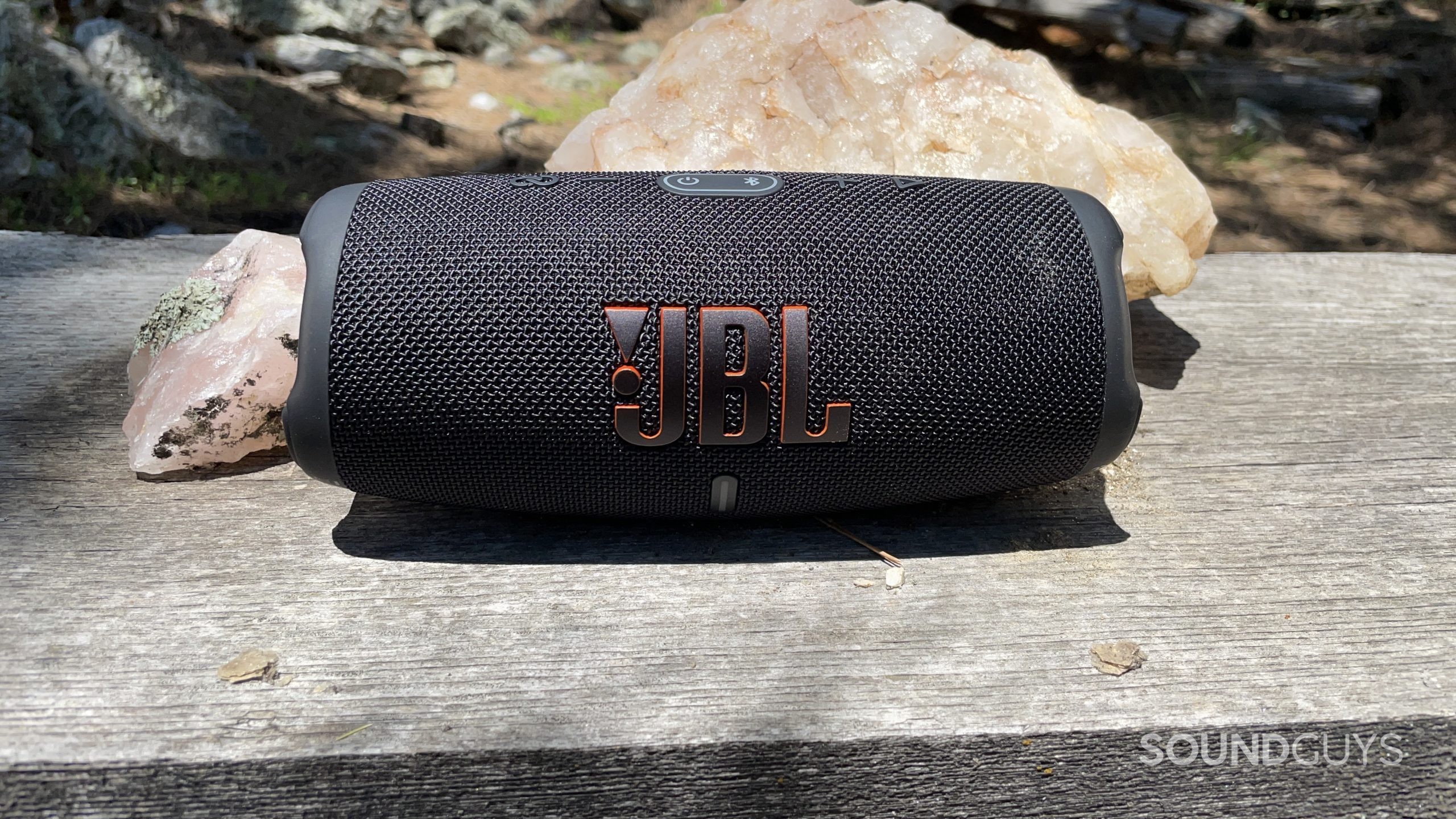JBL Charge 5 resting on a wooden bench with crystals..