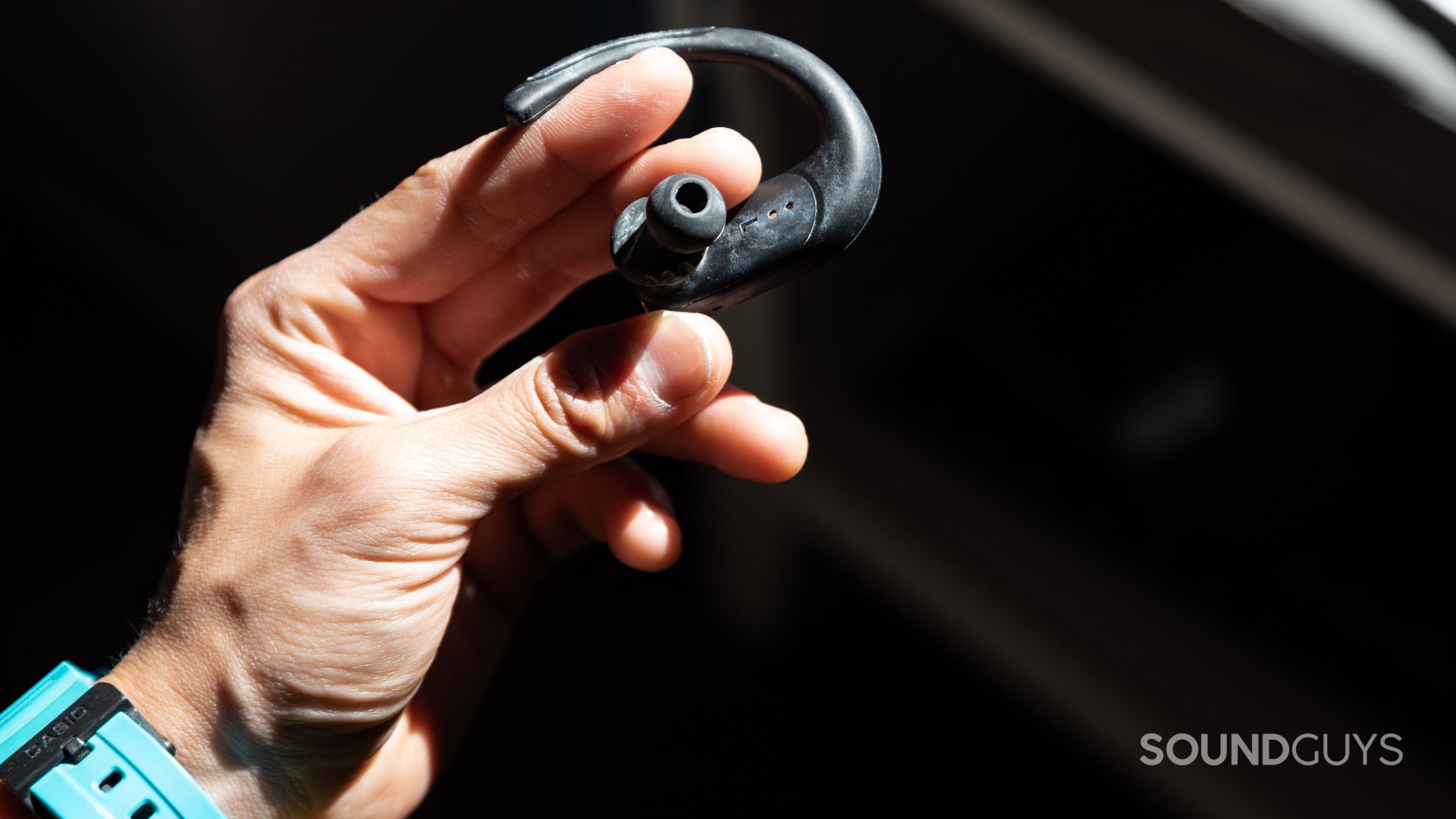A hand holds the JBL ENDURANCE PEAK II true wireless workout earbud by the powerhook, which powers the earbuds on and off.