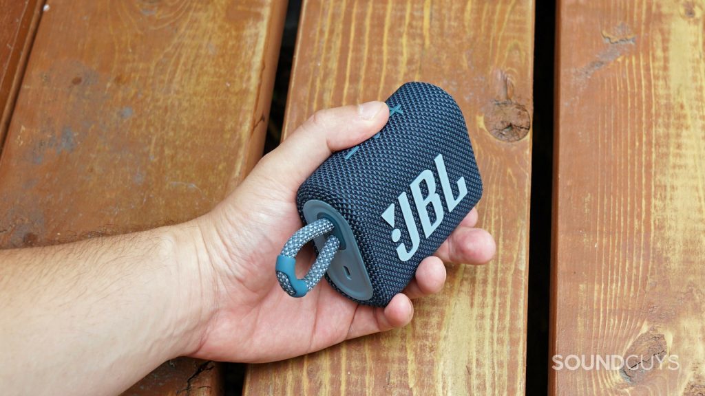 A man holds the JBL Go 3 in front of a wooden surface.