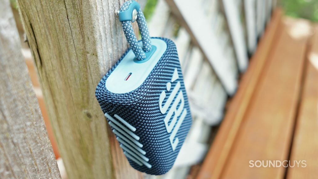 The JBL Go 3 hangs from a screw on a wooden patio divider.