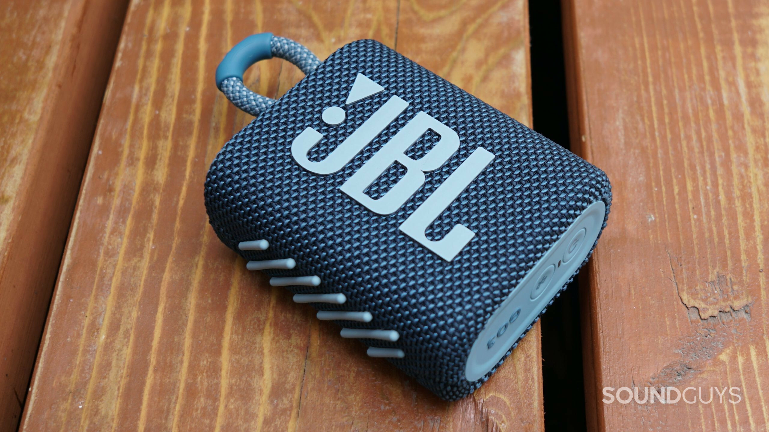 The JBL Go 3 lays on a wooden surface.