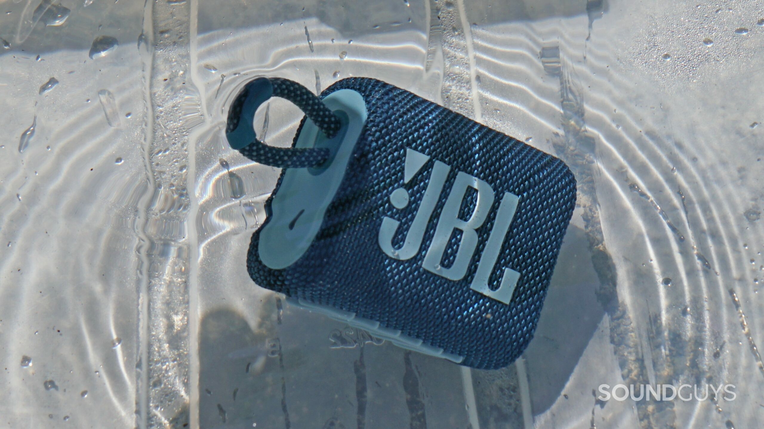 The JBL Go 3 bluetooth speaker submerged in a water outdoors.