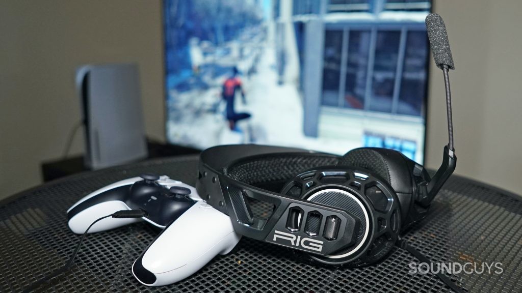 The Nacon RIG 500 Pro HC gaming headset sits on a metal table, leaning on a PlayStation DualSense controller, in front of a PlayStation 5 and a TV running Marvel's Spider-Man: Miles Morales.
