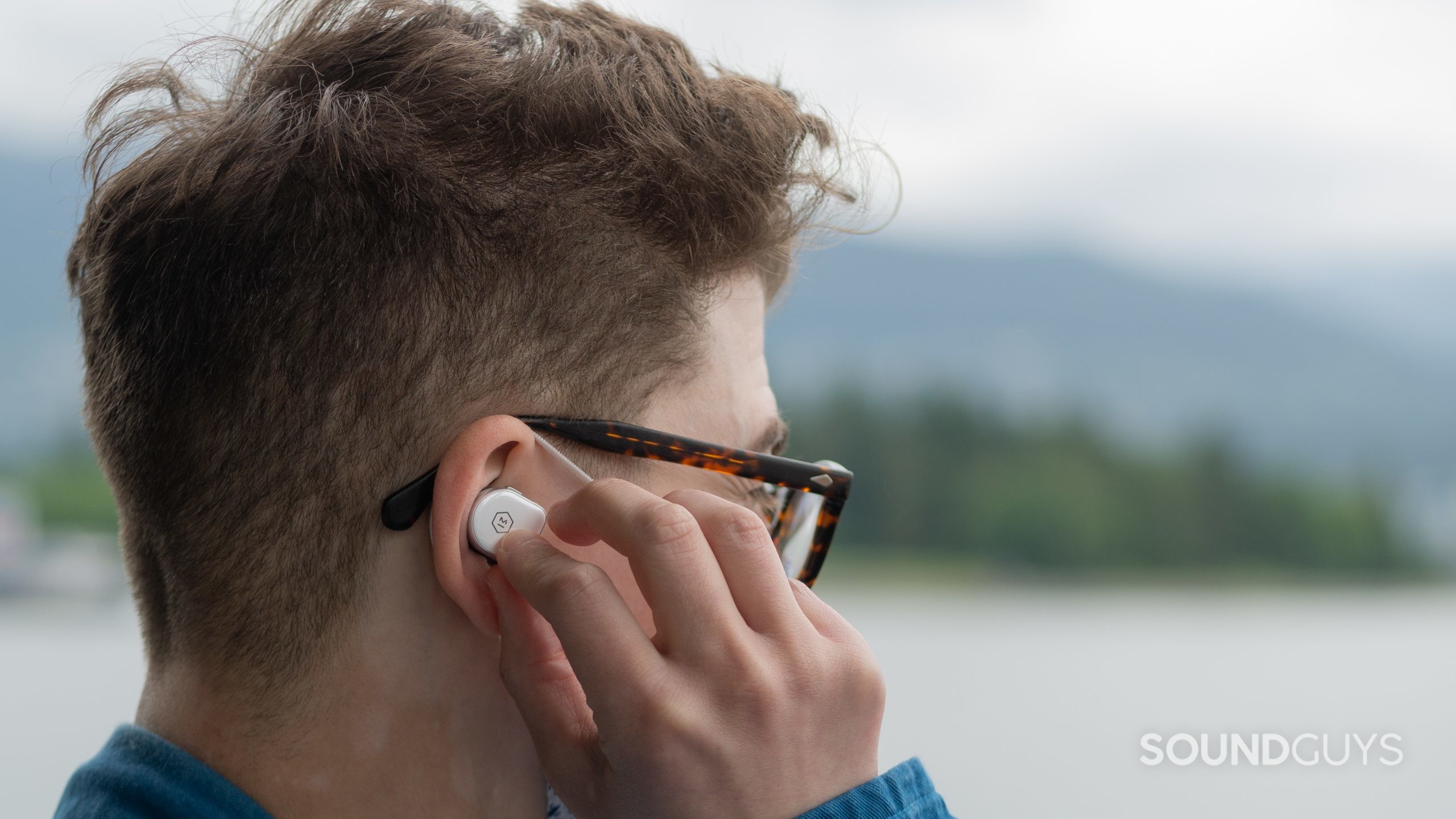 A man holds the master &amp; dynamic MW08 earbud to his right ear.