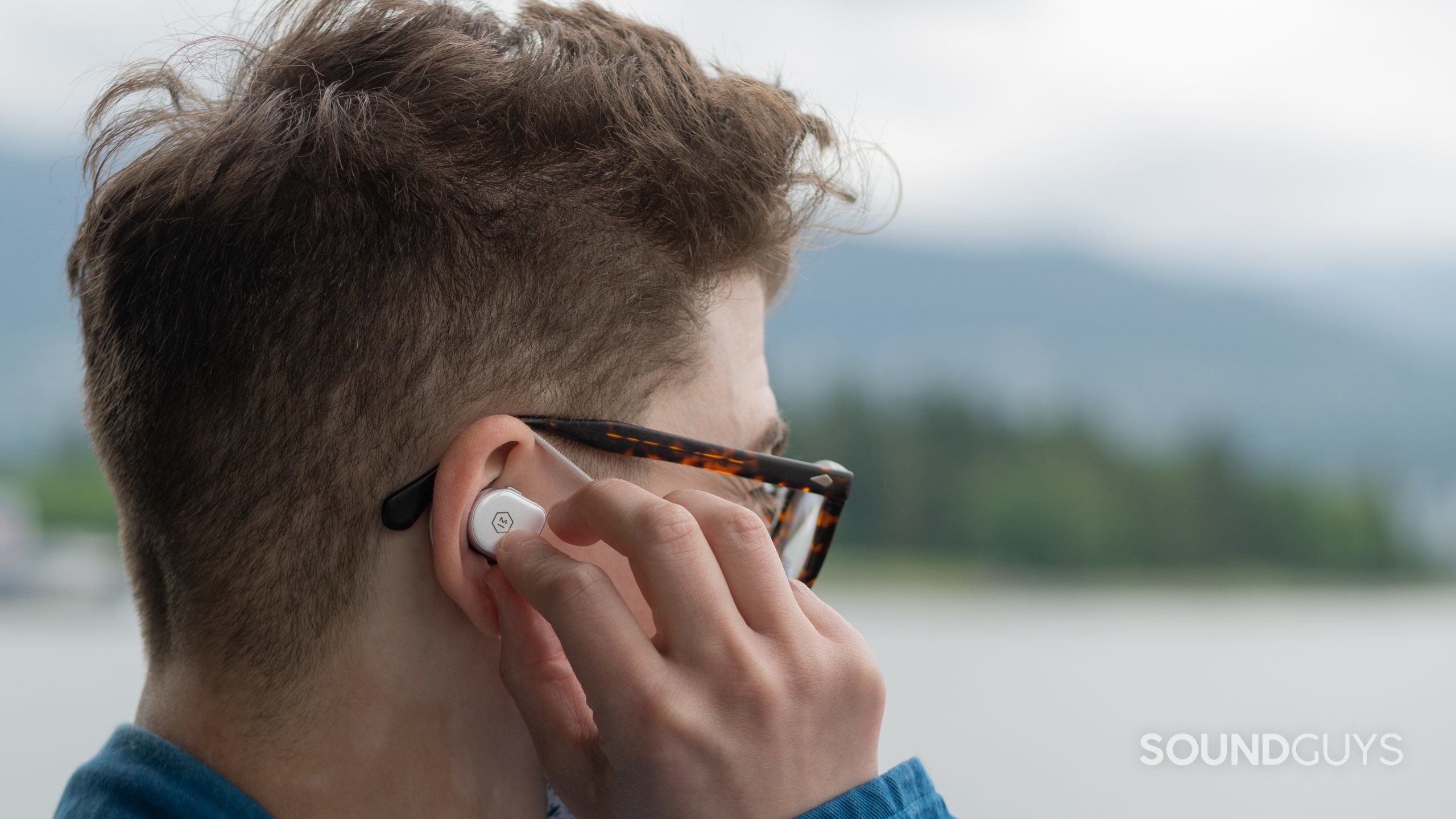 Here's a close up of a man holding master & dynamic MW08 earbud to his right ear.