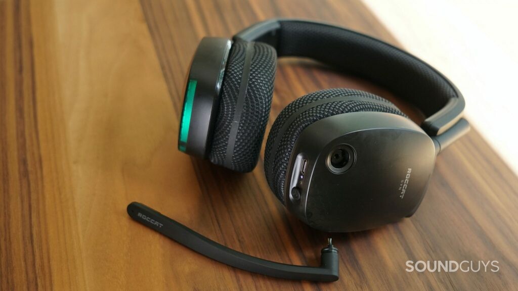 The Roccat Syn Pro Air gaming headset lays on a wooden table with its mic detached, it's charging port and and power button in view.