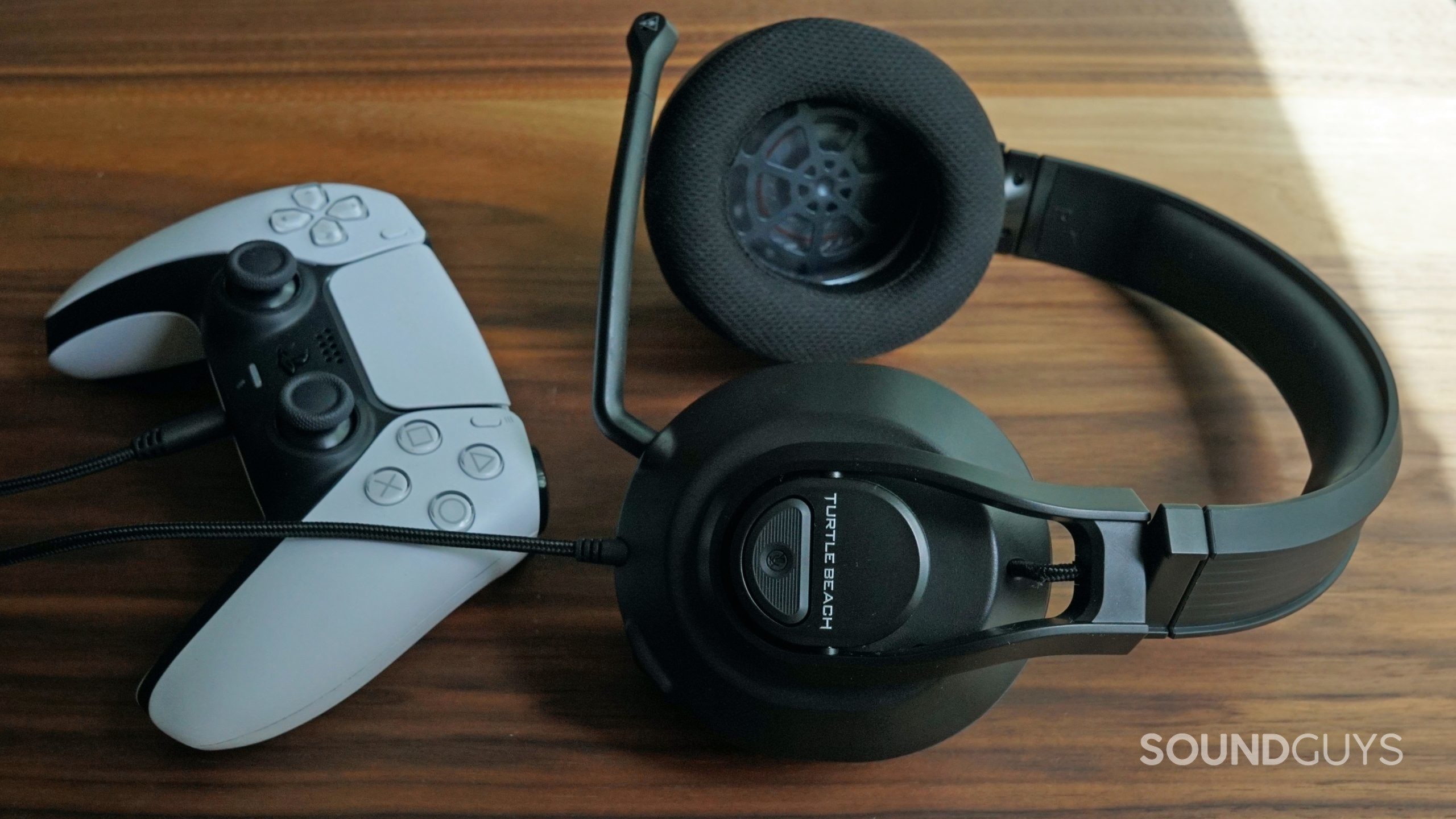 The Turtle Beach Recon 500 lays on a wooden table plugged into a PlayStation DualSense controller.