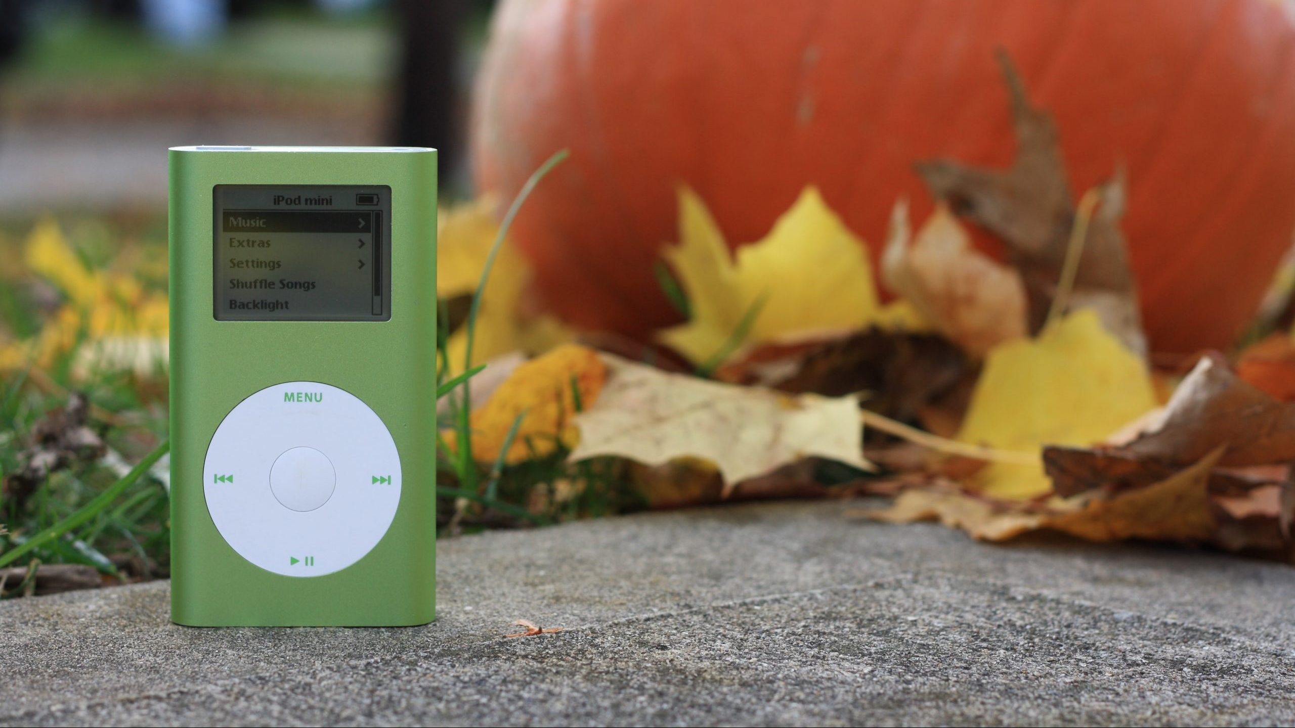 A green apple iPod in front of pumpkin.