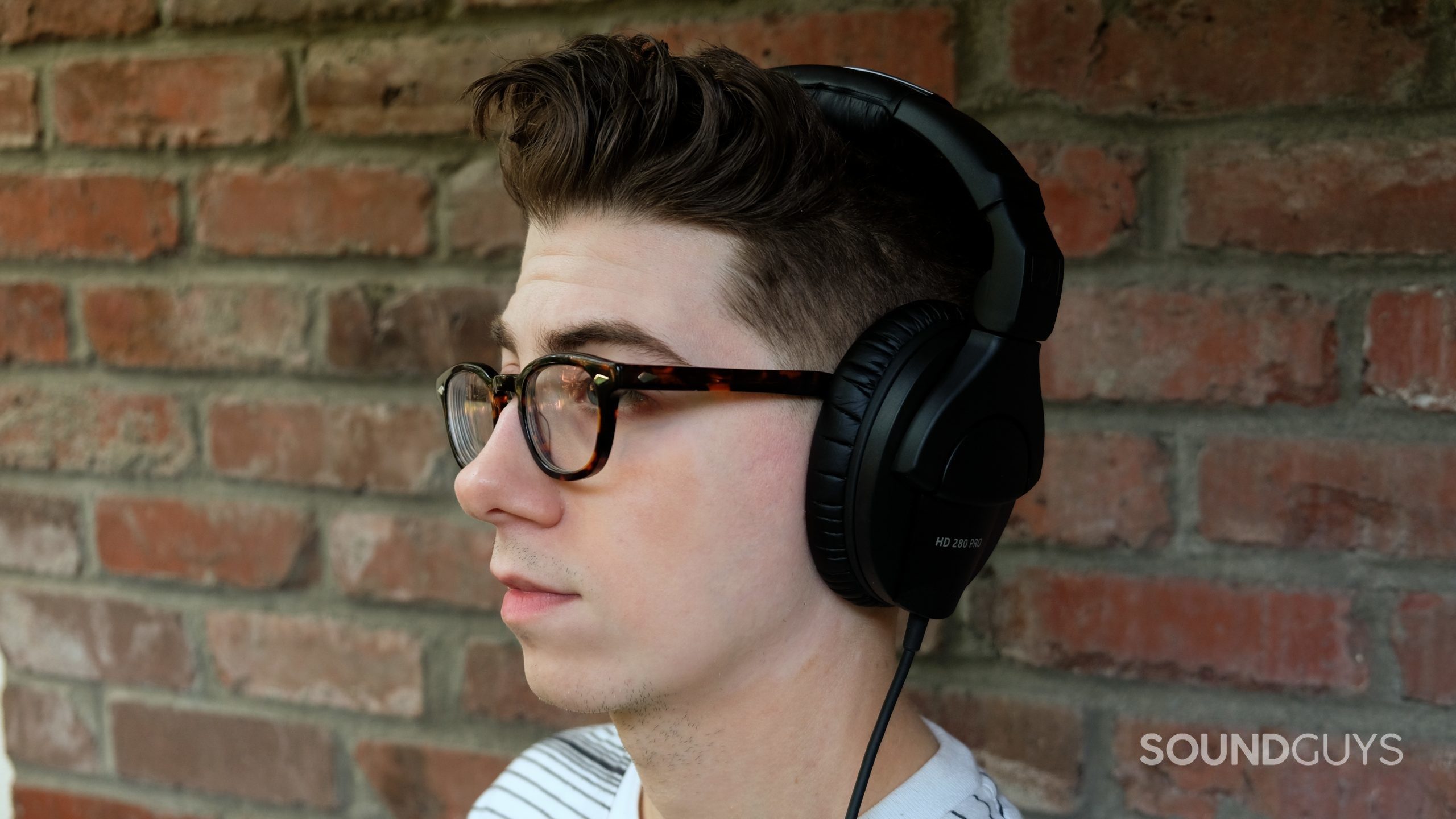 A man wears the Sennheiser HD 280 Pro studio headphones in front of a brick wall.